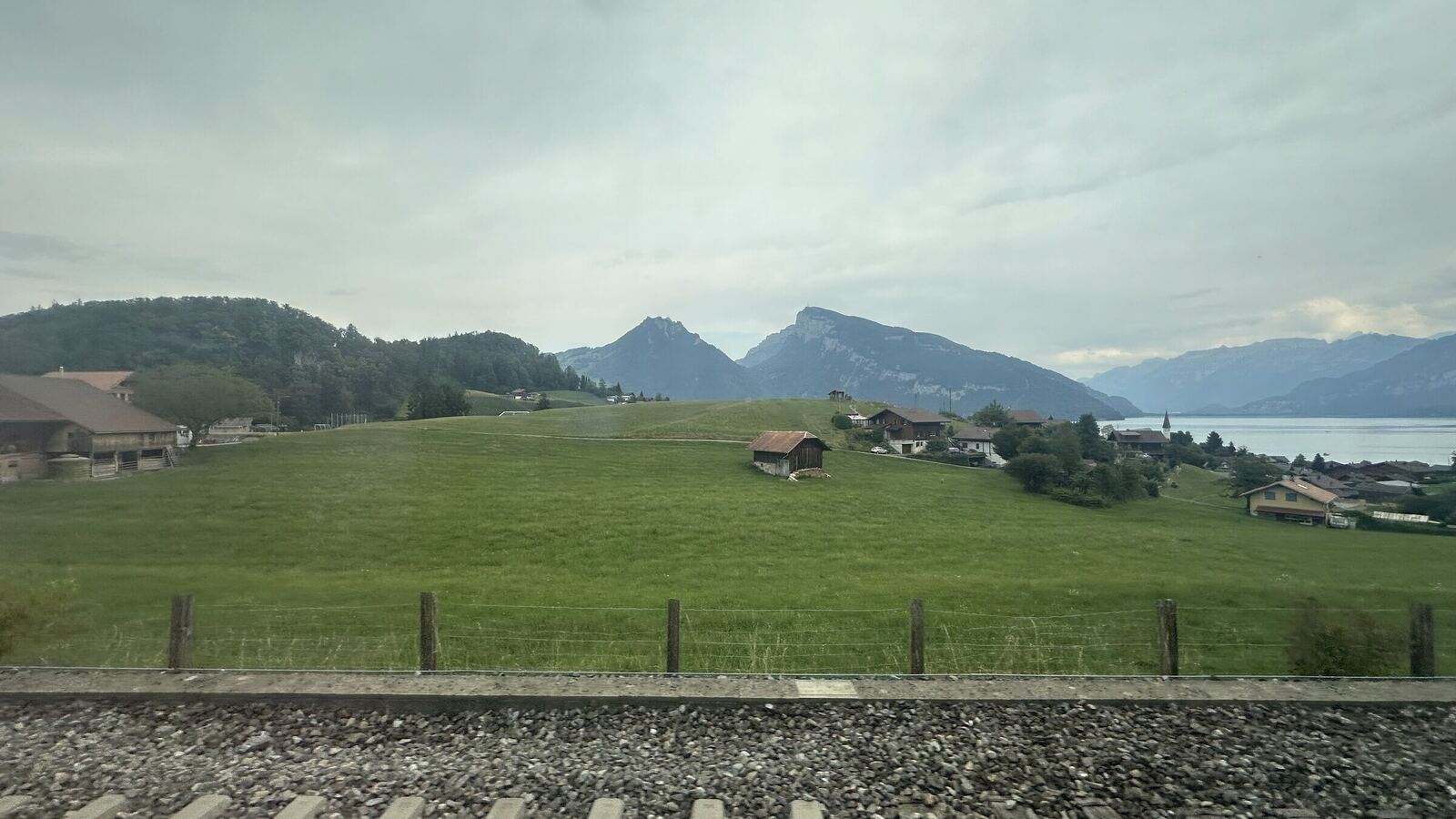 列車の窓から見た草原と山。奥に湖と山並みが見える